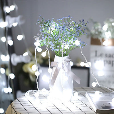 PWO Fitness LED Lights Small Ball Christmas String Light illuminating a vase with flowers on a table.